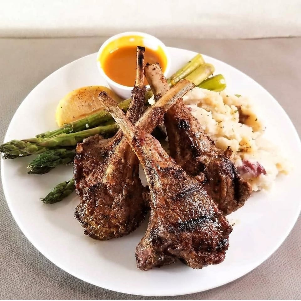 Grilled lamb chops with mashed potatoes, asparagus, lemon, and a side of sauce.