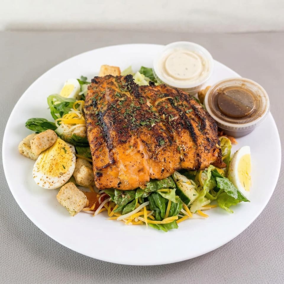 Grilled salmon salad with hard-boiled eggs, croutons, and two dressings on a white plate.